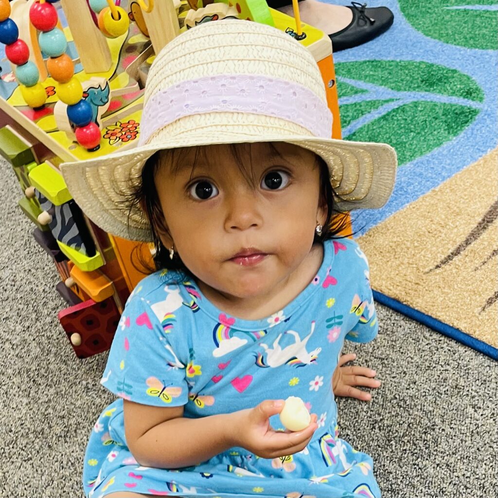 Child wearing hat, playing with toy in playroom.