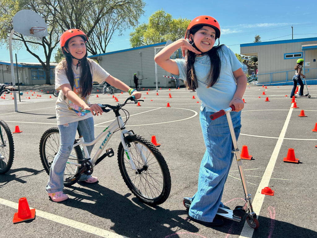 Children riding bike and scooter with helmets outdoors.