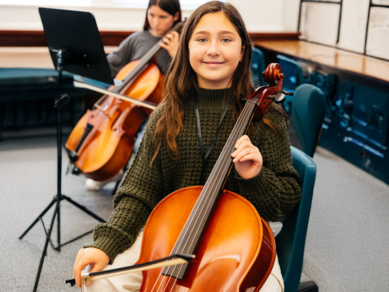 Two girls playing cellos in music class.