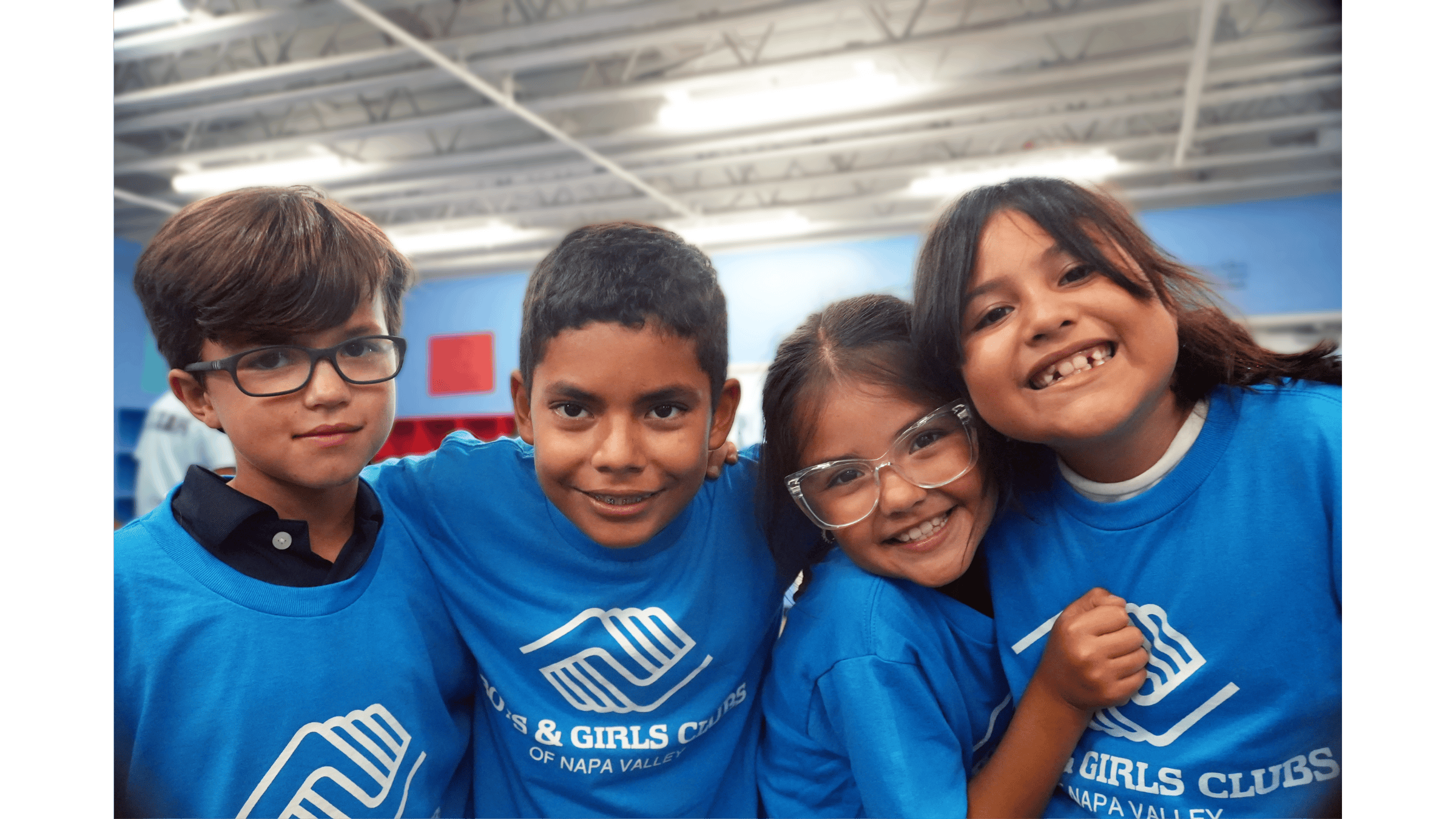 Four smiling children in blue shirts indoors.