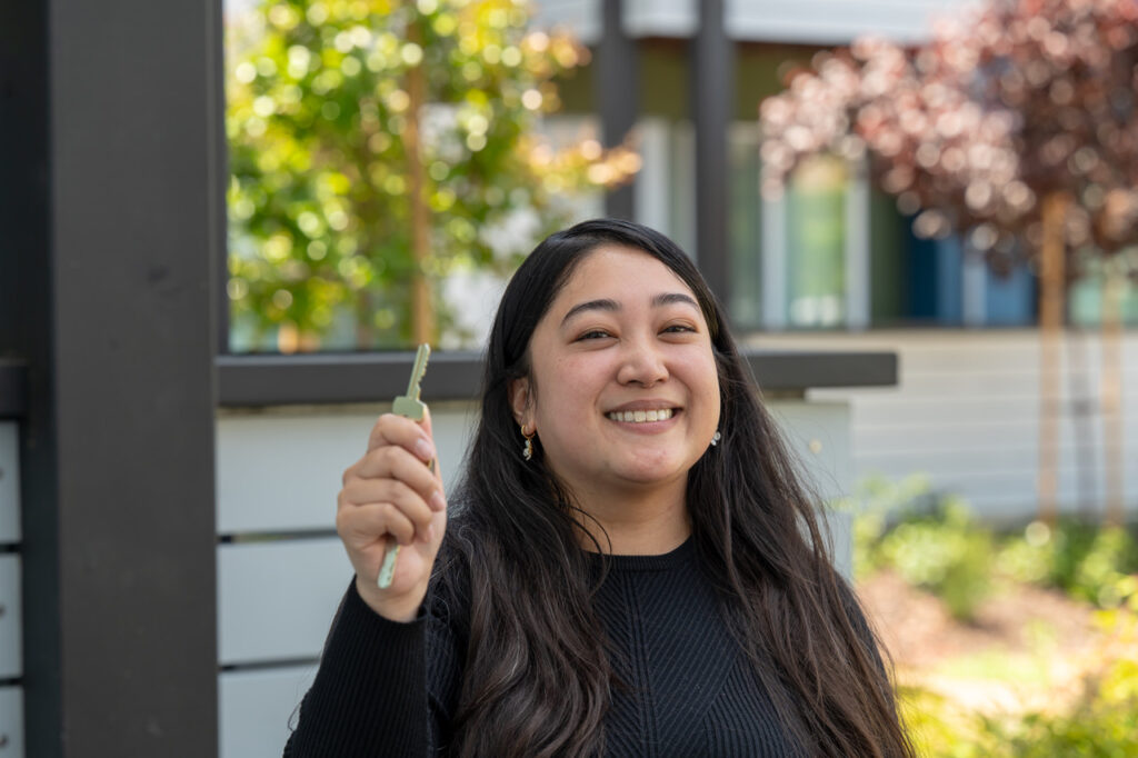 Smiling person holding key outdoors.